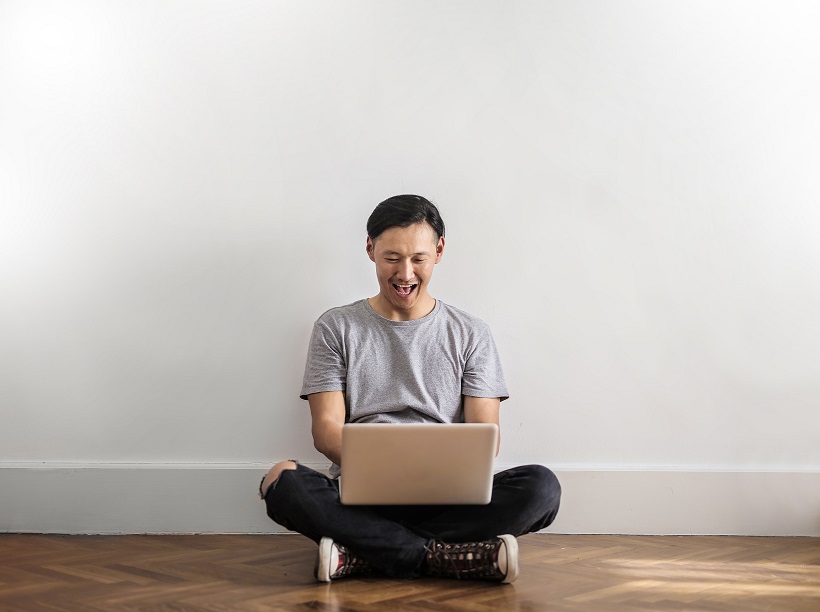A happy man sitting on the floor and typing on his laptop